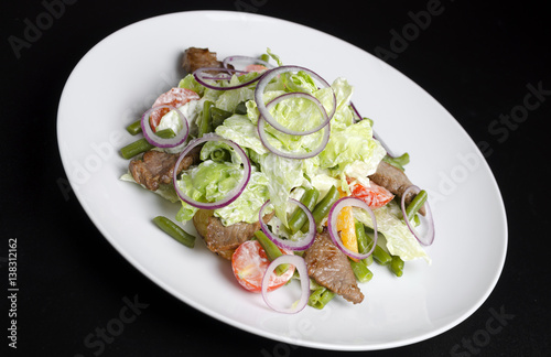 Salad with beef roast beef and vegetables on a black background