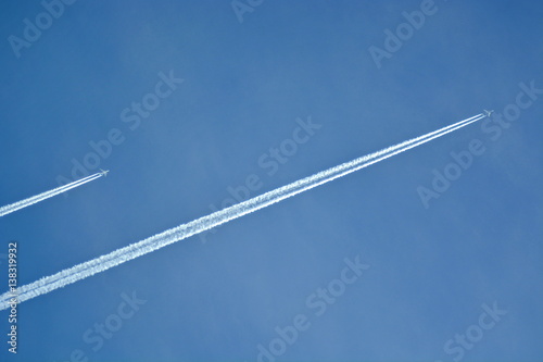 a pair of aircraft flying in the clear sky diagonally leaving a white trail