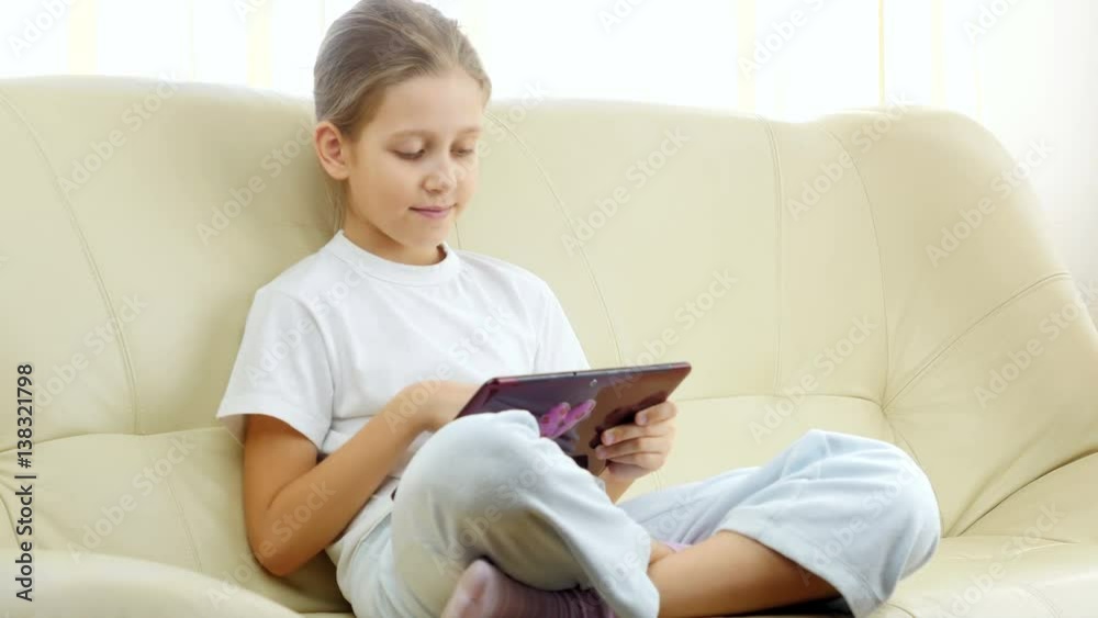 Seven years old girl with tablet PC. Girl relaxing on sofa using touchpad looking at camera. Seven years old girl with tablet PC. Girl relaxing on sofa using touchpad looking at camera.