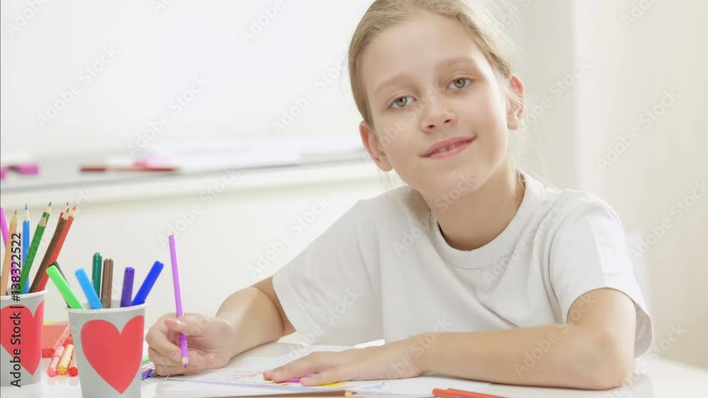 Seven years old girl drawing and coloring on a paper at home. Girl looking at camera and smiling. Seven years old girl drawing and coloring on a paper at home. Girl looking at camera and smiling.