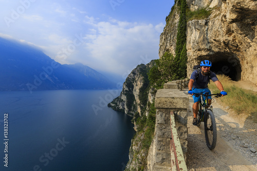 Mountain biking at sunrise man over Lake Garda on path Sentiero della Ponale, Riva del Garda, Italy