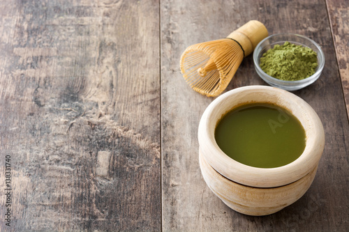 Matcha green tea in a bowl and bamboo whisk, on wooden background 