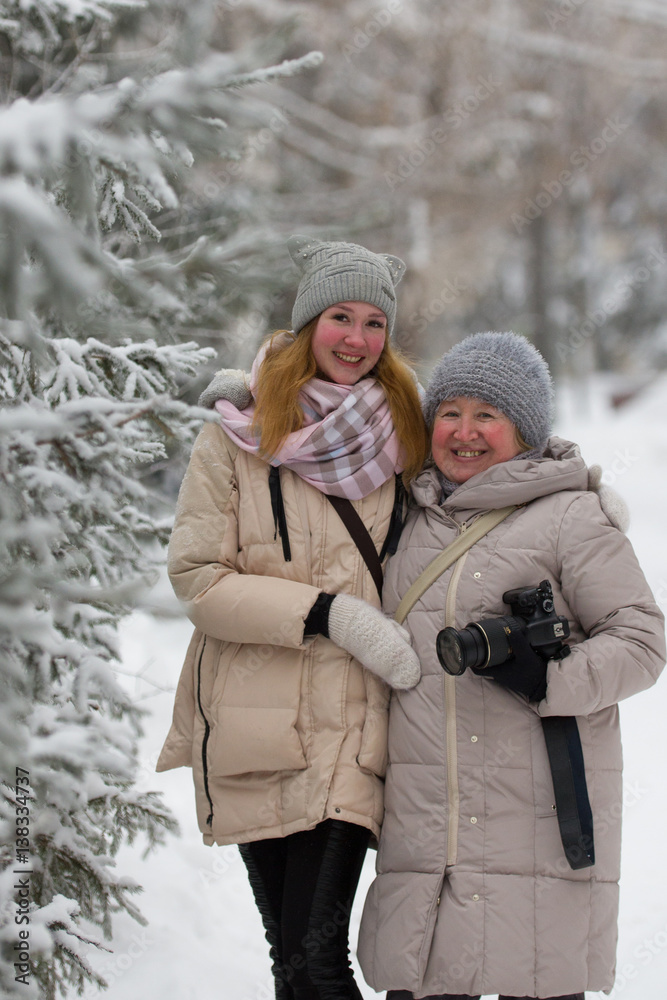 Young woman and adult female in winter park - standing near snow-covered pines