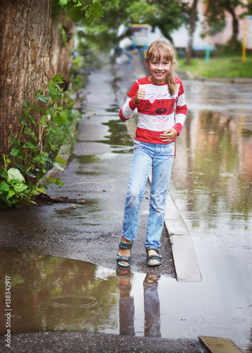 A girl stands near a puddle in the rain.