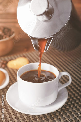 Fresh coffee pouring from pot into cup