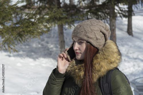 Beautiful girl in winter clothes in the park talking on the phone with a serious expression on his face photo