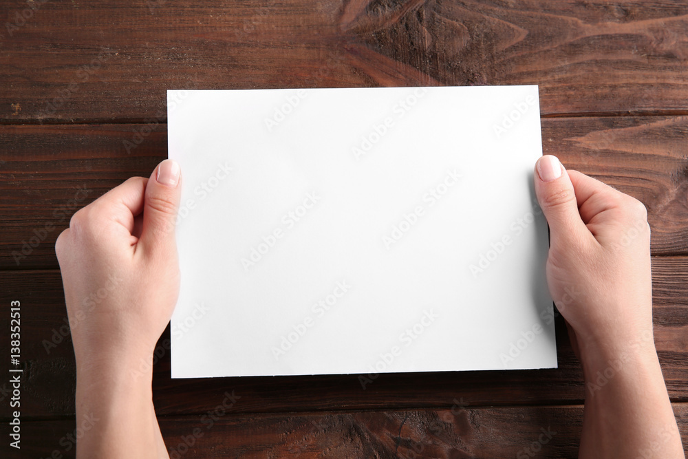 Female hands holding empty paper sheet on wooden background Female hands holding empty paper sheet on wooden background