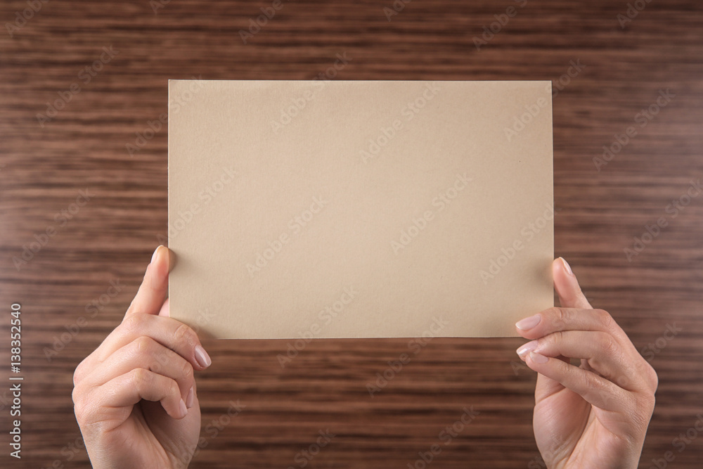 Obraz premium Female hands holding empty paper sheet on wooden background