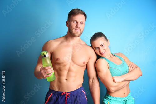 Sporty young couple with bottle of water on color background