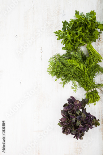 Parsley, dill and basil on a light wooden background.