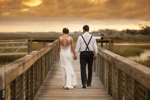 Beautiful newly married couple walking away with dramatic sky photo