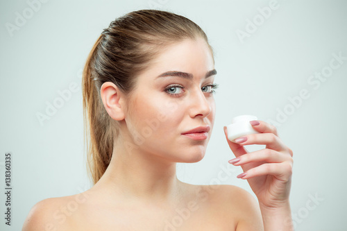Portrait of young beautiful woman applying moisturizing cream on her face