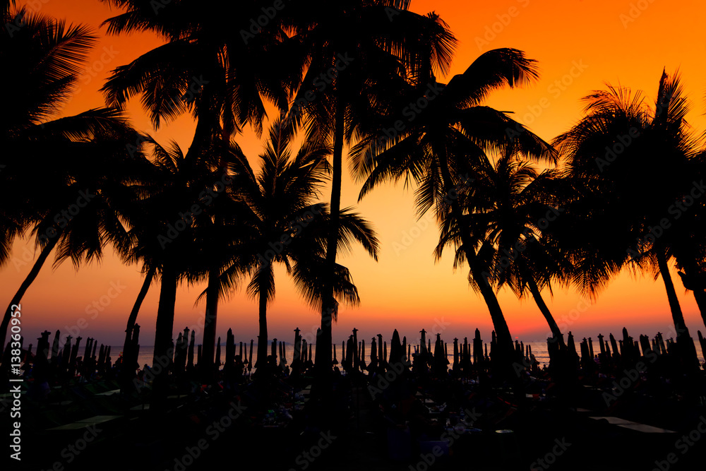 Dark silhouettes of palm trees and beach umbrella with amazing cloudy sky sunset at tropical beach in Pattaya Thailand. Coconut Tree with Beautiful and romantic sunset in Maldives island. color filter