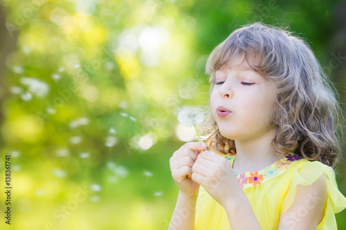 Happy child blowing dandelion flower outdoors