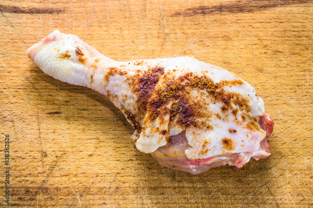 Raw chicken leg with spices on wooden cutting board, ready for frying or cooking, top view