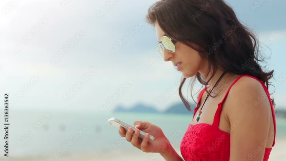 Attractive young woman using her phone on the beach in slow motion Attractive young woman using her phone on the beach in slow motion