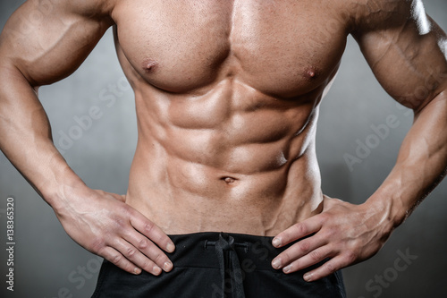 Brutal strong bodybuilder man posing in studio on grey background