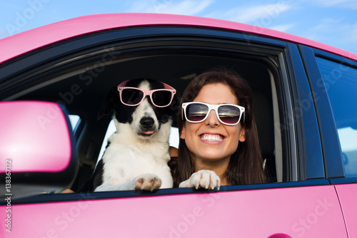 Woman and dog in pink car on summer road trip vacation. Funny dog with sunglasses traveling. Travel with pet concept. © Dirima