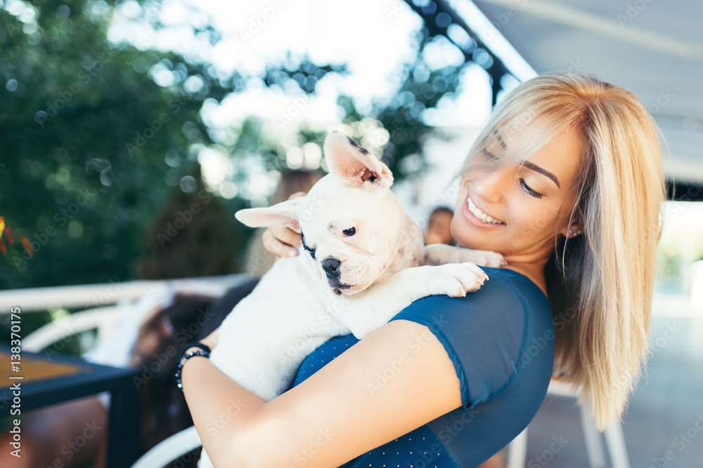 Beautiful young woman sitting in cafe with her adorable French bulldog puppy. Spring or summer city outdoors. People with dogs theme. Beautiful young woman sitting in cafe with her adorable French bulldog puppy. Spring or summer city outdoors. People with dogs theme.