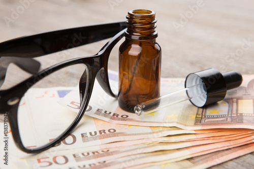 eye care concept - reading glasses, eye drops and money