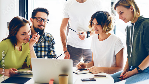 Team of analysts of the modern start up are discussing the business strategy for the next year in the modern and bright office. Young hipsters are sitting with the electronic devices during meeting.