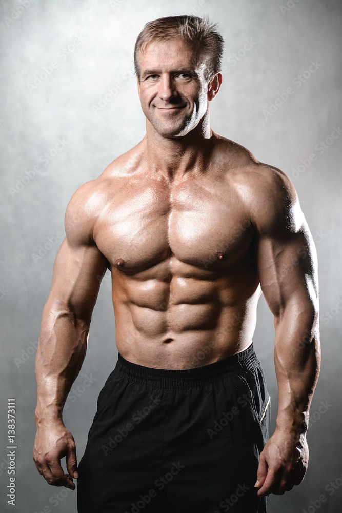 Brutal strong bodybuilder old man posing in studio grey background