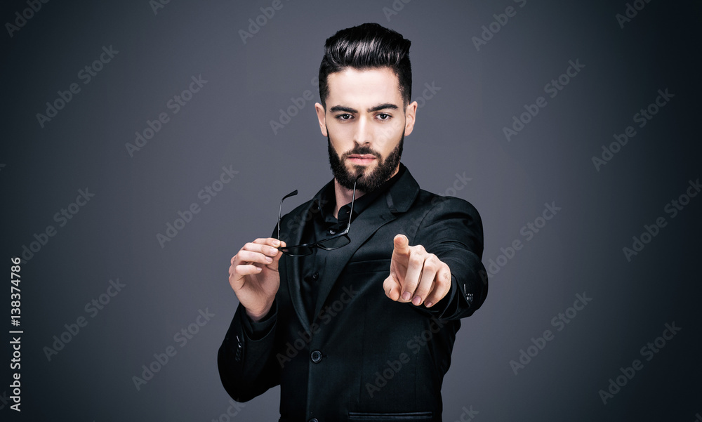 Portrait d'un jeune homme d'affaires, une paire de lunettes dans une main, pointant du doigt l'objectif Portrait d'un jeune homme d'affaires, une paire de lunettes dans une main, pointant du doigt l'objectif