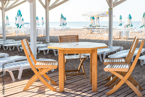 Wooden furniture in the restaurant on the beach, table and chairs made of solid wood on a background of sea and sun loungers © markhipov