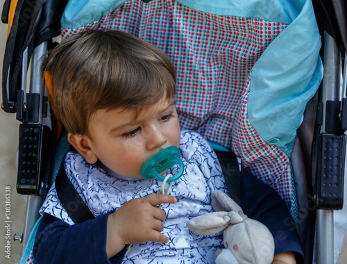 A kid with a pacifier in his baby carriage photo