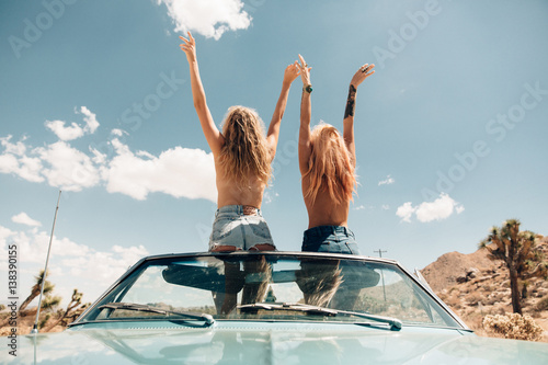 Rear view of women topless in convertible car arms raised