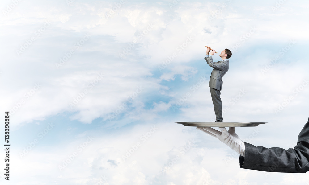 Businessman on metal tray playing fife against blue sky background Businessman on metal tray playing fife against blue sky background