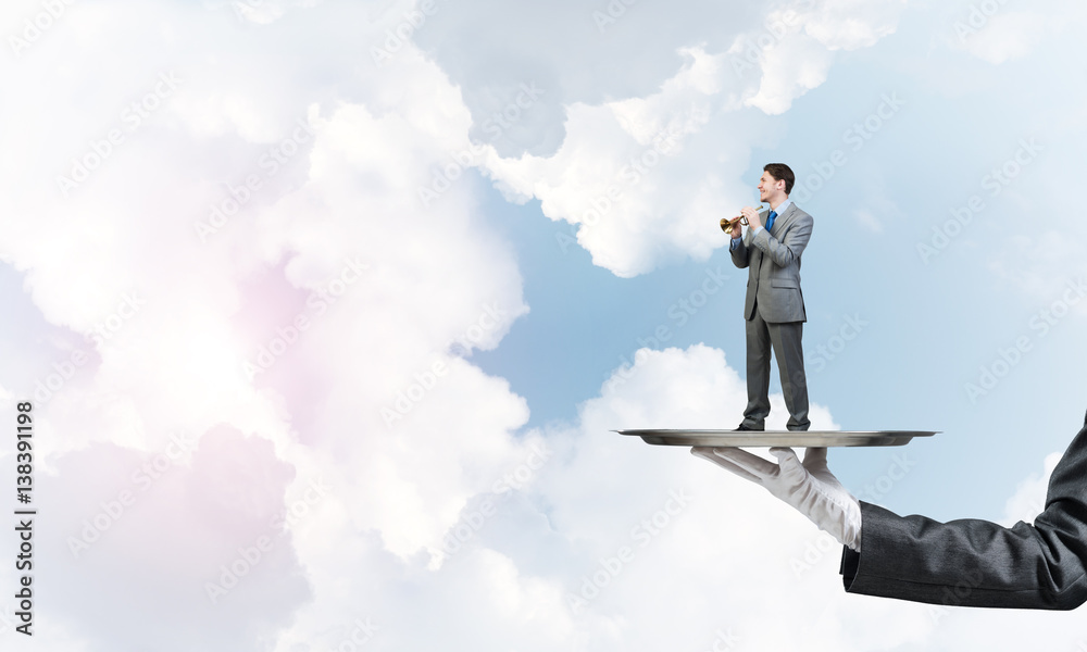 Businessman on metal tray playing fife against blue sky background Businessman on metal tray playing fife against blue sky background
