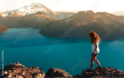 Woman walking by lake and snow capped mountains, Garibaldi Provincial Park, British Columbia, Canada 