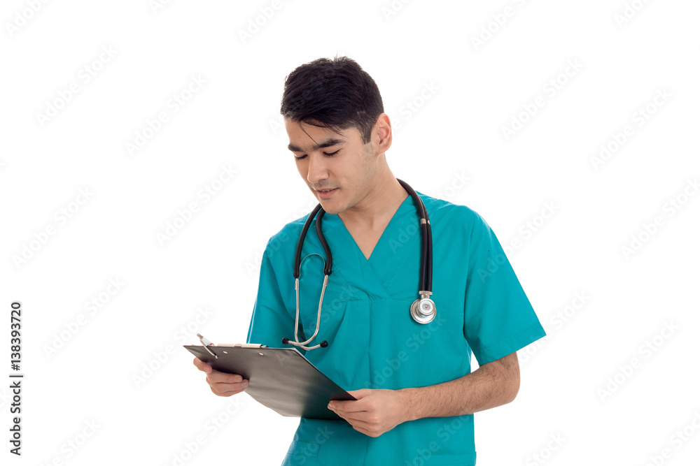 portrait of handsome brunette male doctor in blue uniform with stethoscope posing and making notes isolated on white background portrait of handsome brunette male doctor in blue uniform with stethoscope posing and making notes isolated on white background