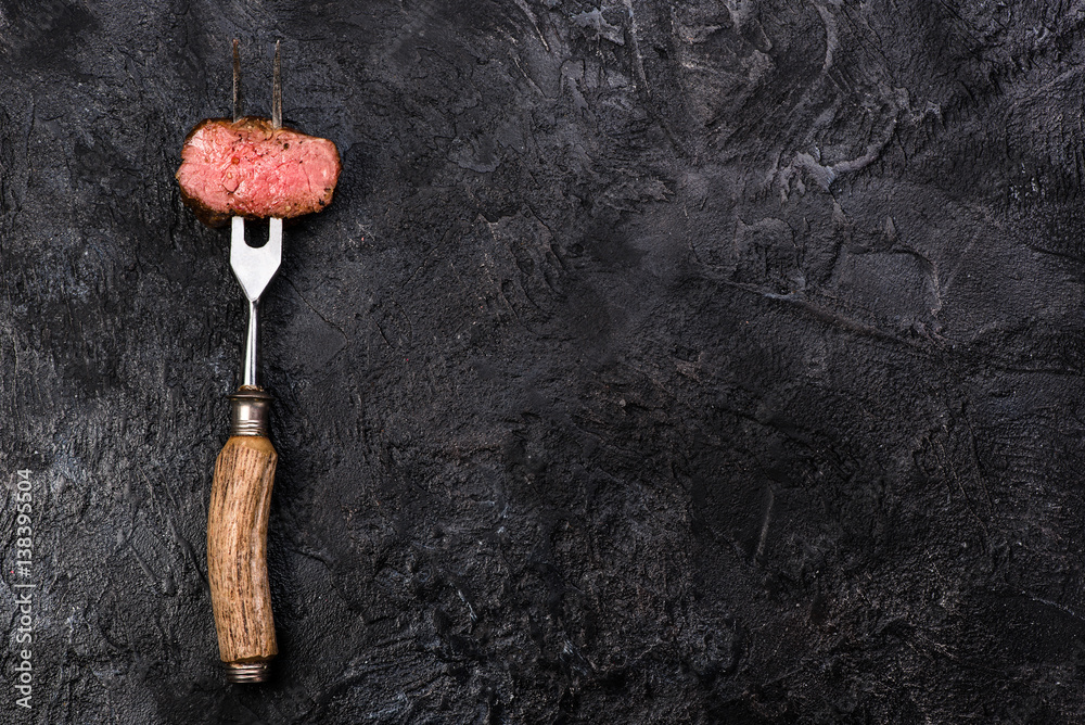 Slices of roast beef on meat fork on dark black background with copy space. Top view.