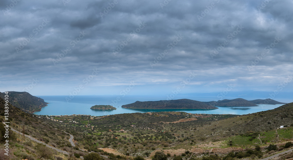 View of the island of Spinalonga with clouds and calm sea. Spinalonga (Crete) is an island where were isolated lepers, and here took place the story of Victoria 's Hislop novel 