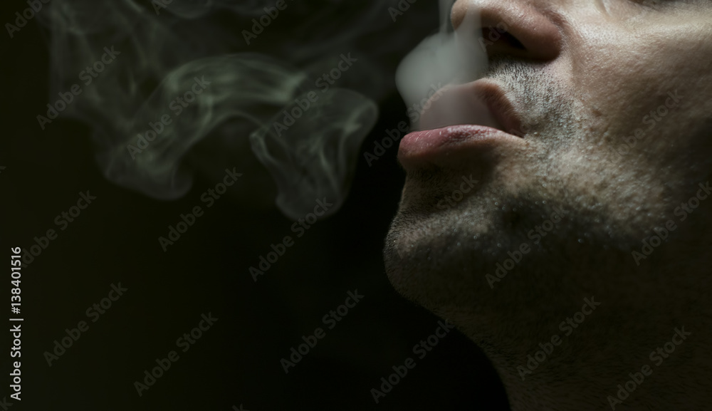 Close up shot of a man exhaling cigarette smoke on black background with dramatic light. Close up shot of a man exhaling cigarette smoke on black background with dramatic light.
