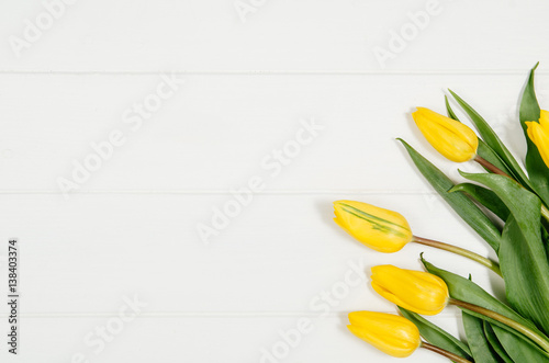 Fototapeta Naklejka Na Ścianę i Meble -  Background with yellow tulips on white wooden table top view. Creative woman's workspace concept with copy space. Product photograph taken from above with frame composition