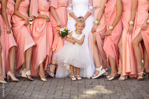 Fotografie Stylish wedding, little girl- bride's sister holding wedding bouquet near legs of bridesmaids