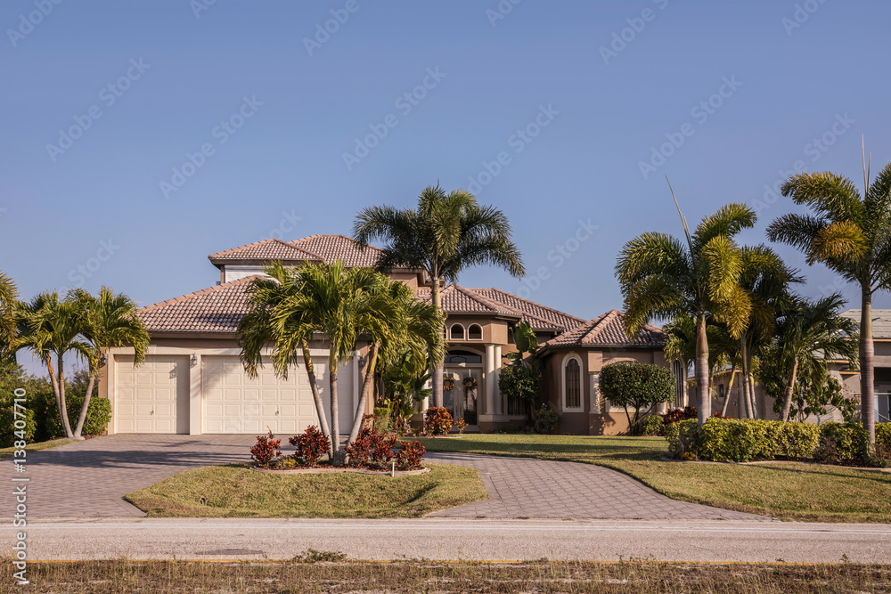 Typical Southwest Florida concrete block and stucco home in the countryside with palm trees, tropical plants and flowers, grass lawn and pine trees. Florida