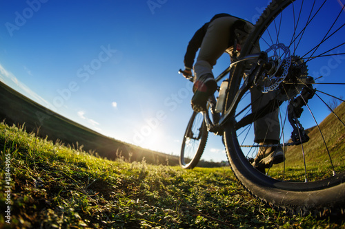 Detail of cyclist man feet riding mountain bike on outdoor trail in sunny meadow