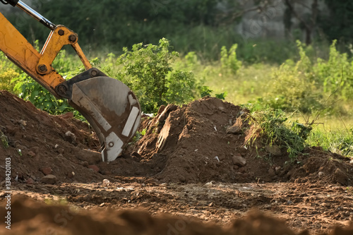 Excavator is working with dusty red soil.