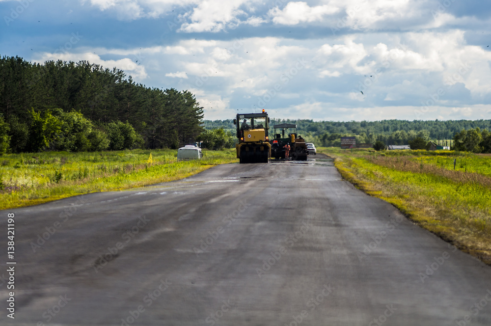 Brigade road workers laying asphalt on the road in the summer with the help of special equipment asphalt paver