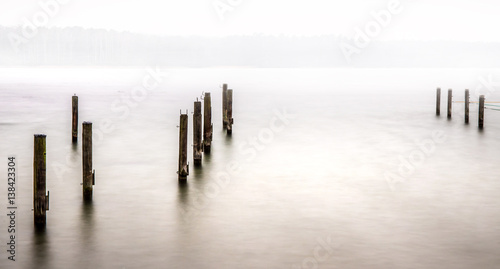 der Hafen eines einsamen Sees liegt im Nebel, einige Pfähle stehen im Wasser