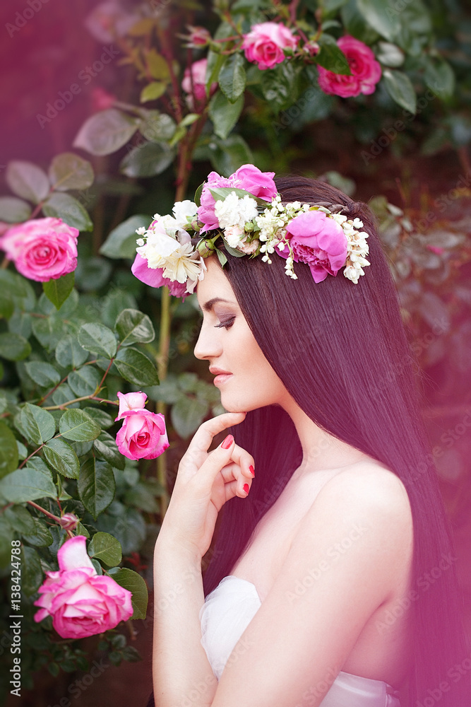 Beautiful Brunette Bride near a Flowering Bush Roses Posing in a Wedding Dress