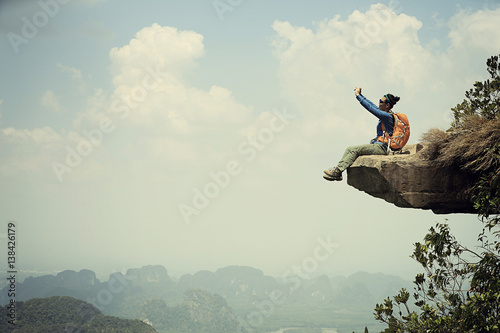 successful woman hiker taking photo with smartphone on mountain peak cliff