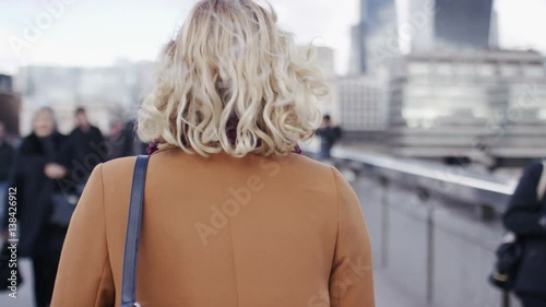 4K Camera follows a young blonde female walking in the city, in slow motion