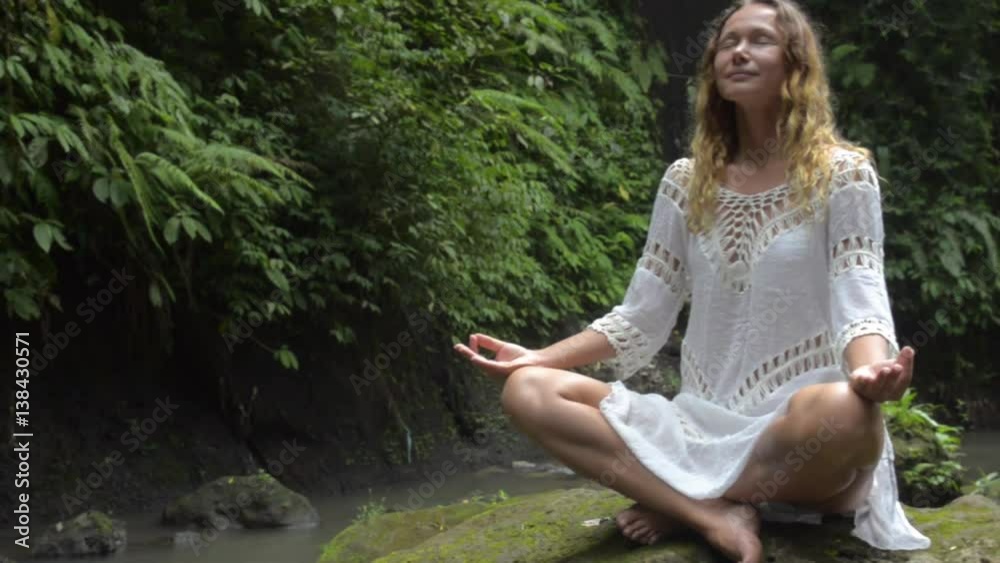 woman doing sitting meditation at waterfall in the tropics