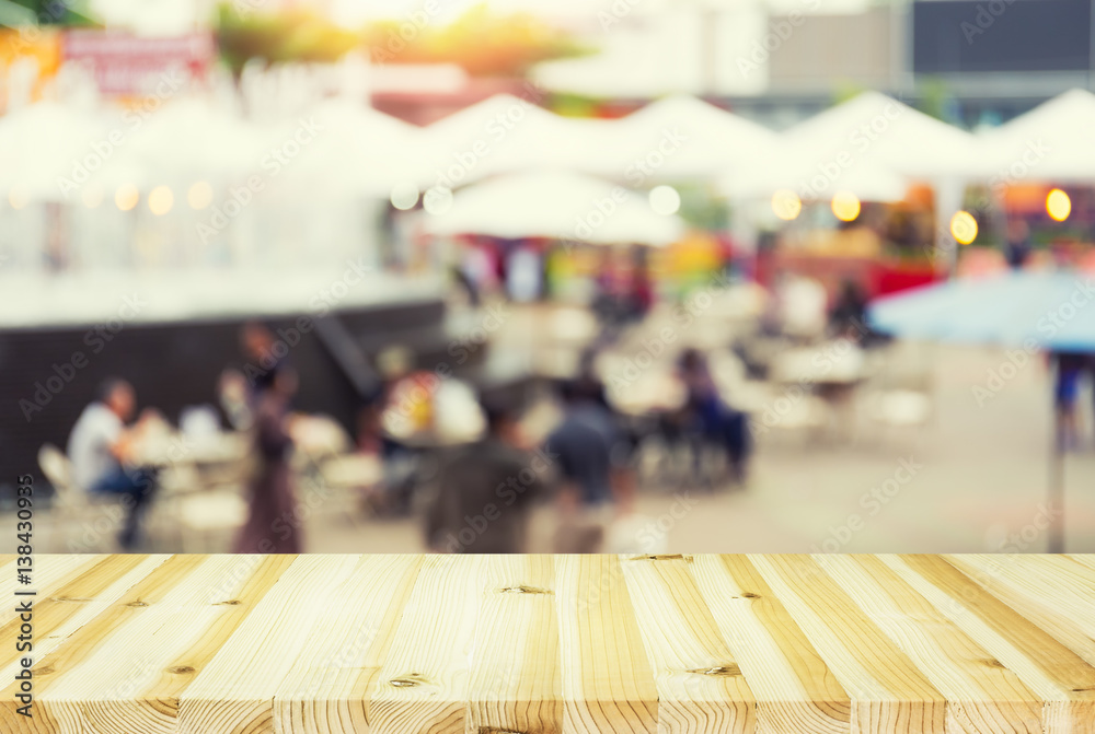 Blurred image of food fairs and food festivals consist of many booth and vendors at food stalls. People walking in street. Event in Chiang Mai at twilight montage with wood table top for background. Blurred image of food fairs and food festivals consist of many booth and vendors at food stalls. People walking in street. Event in Chiang Mai at twilight montage with wood table top for background.