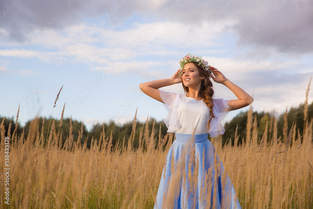 Girl with circlet of flowers walking in golden dried grass field Girl with circlet of flowers walking in golden dried grass field